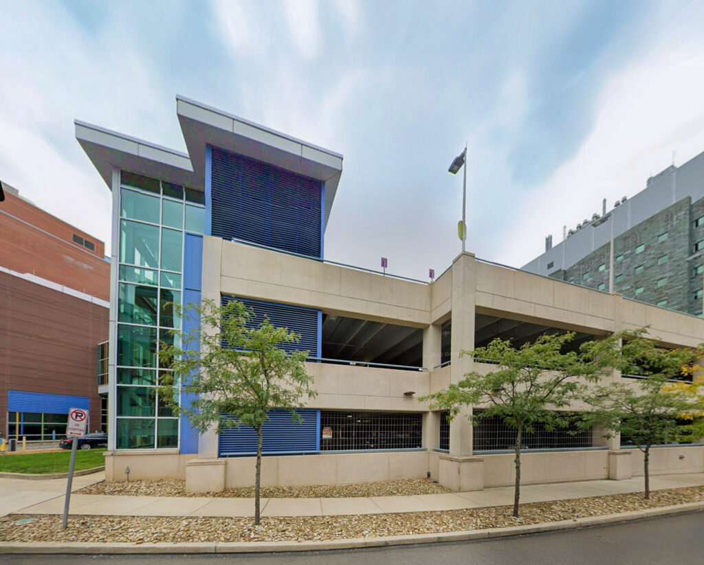 A multi-level concrete parking garage with a modern glass stairwell tower and blue accents.