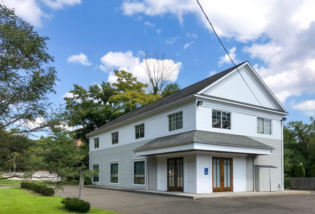 A two-story white building with horizontal siding and a covered entrance with glass double doors.