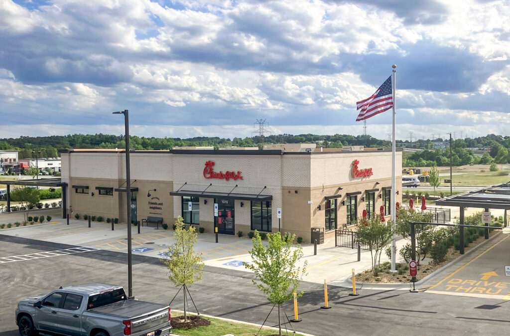 A Chick-fil-A restaurant building with a parking lot and an American flag on a pole.