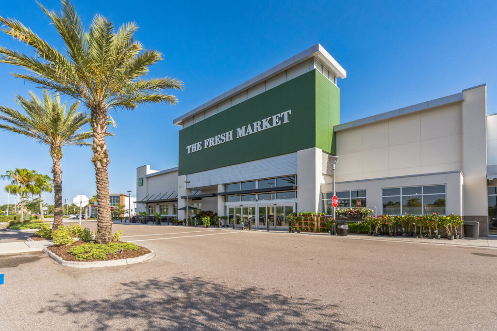 The Fresh Market storefront with potted plants displayed outside the entrance.