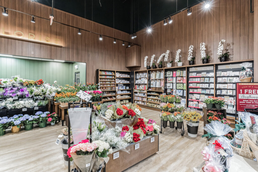 Interior view of a flower shop with shelves of greeting cards, gift items, and buckets of assorted fresh-cut flowers.