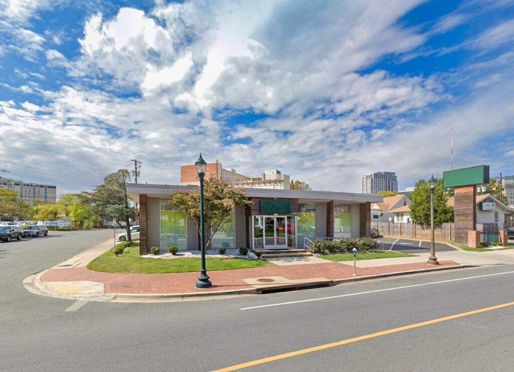 A single-story commercial building on a street corner with a small parking lot and a tall blank sign post.
