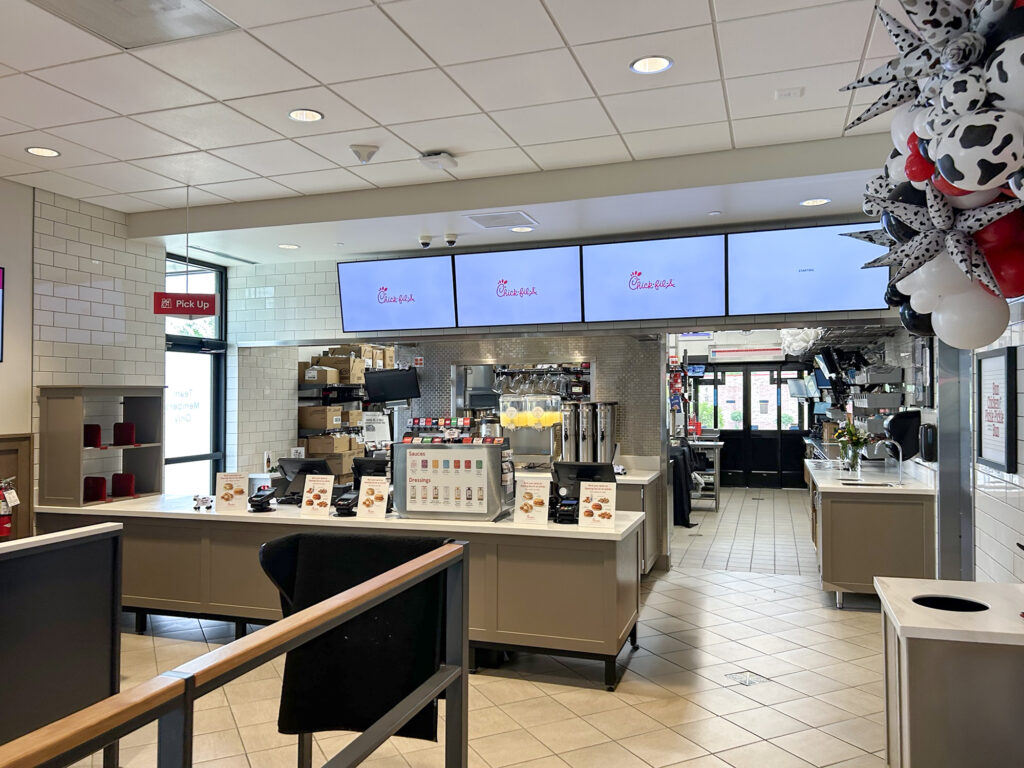 Interior of a Chick-fil-A restaurant featuring a service counter, digital menu boards, and a balloon arch on the right.
