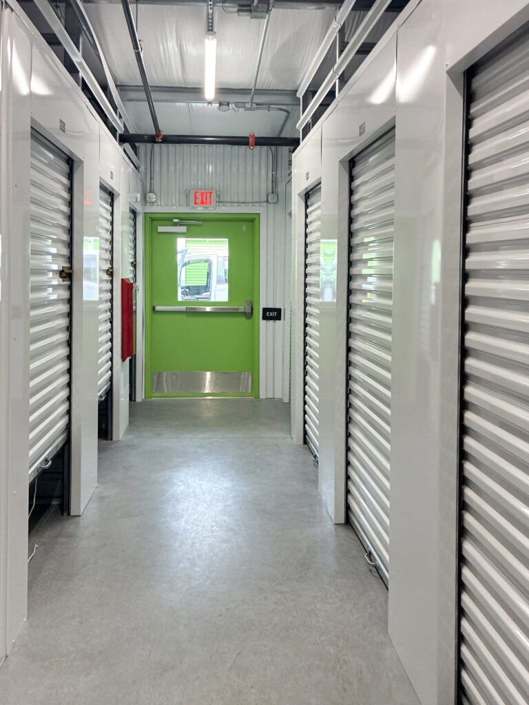 A hallway lined with white storage unit doors leading to a green emergency exit door.