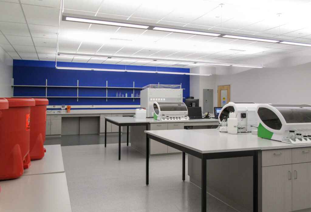 Laboratory interior with workbenches, analytical equipment, and two red biohazard bins in the foreground.