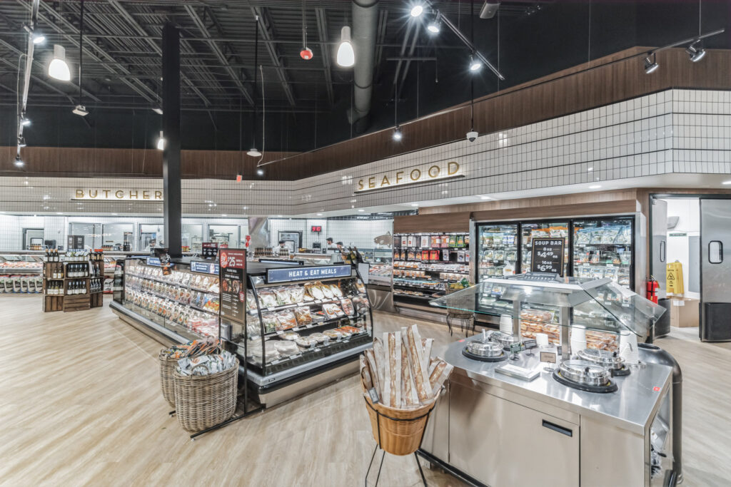 Interior view of a grocery store meat and seafood department featuring refrigerated display cases, a soup bar, and baskets of packaged goods.