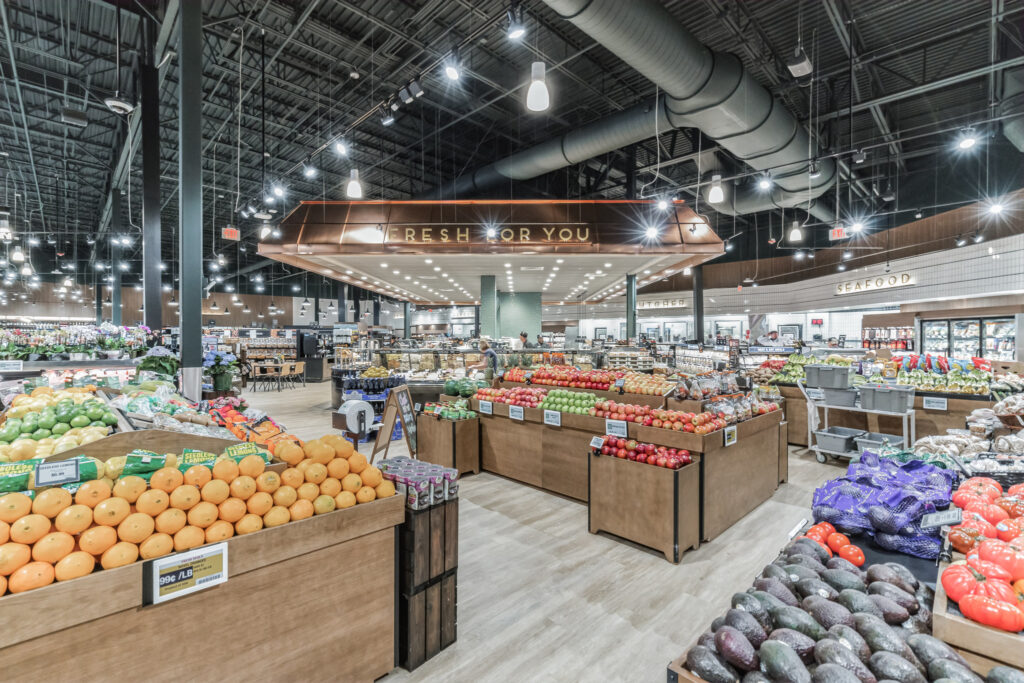 Produce section of a grocery store with bins of oranges, lemons, apples, and avocados, featuring a sign reading “Fresh for You.”