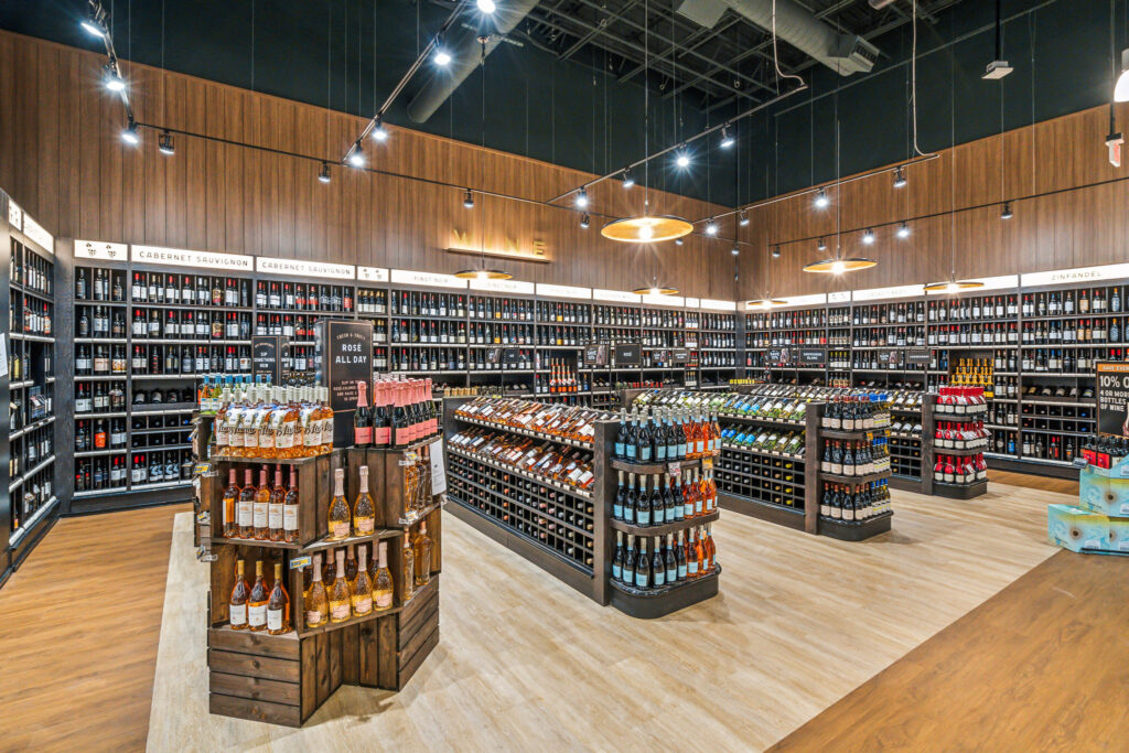 Interior of a wine shop with aisles of wooden shelves stocked with various bottles of wine, including a front display of rosé.