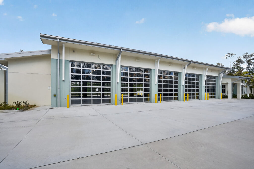 A modern commercial building featuring five large glass garage-style doors and a wide concrete driveway.