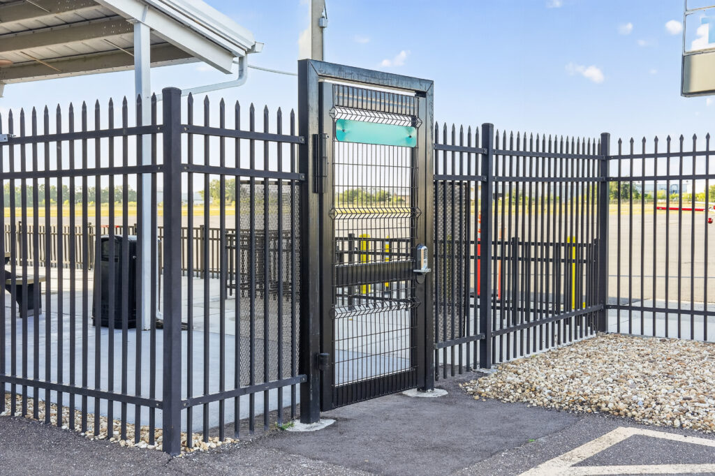 A black metal perimeter fence with a central gate and a blank green sign above the doorway.