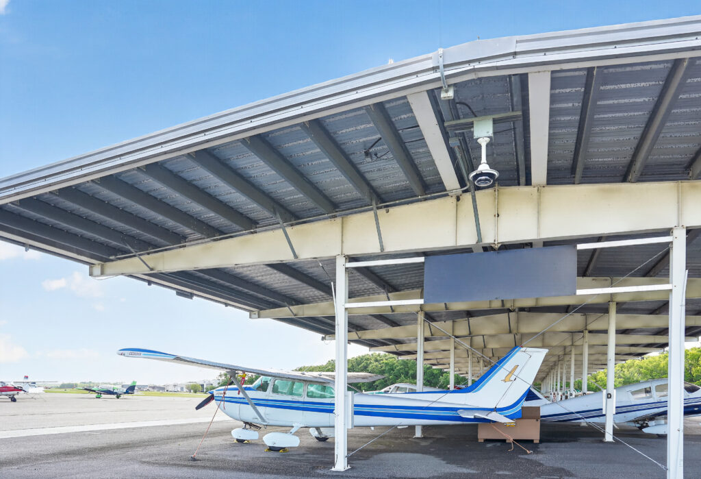 A white and blue single-engine propeller plane parked under a metal airport canopy.
