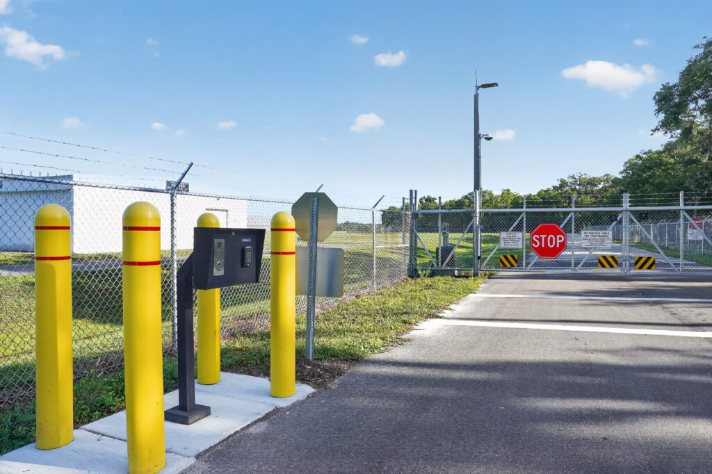 Gated entrance to a restricted area with a keypad, yellow bollards, and a stop sign.