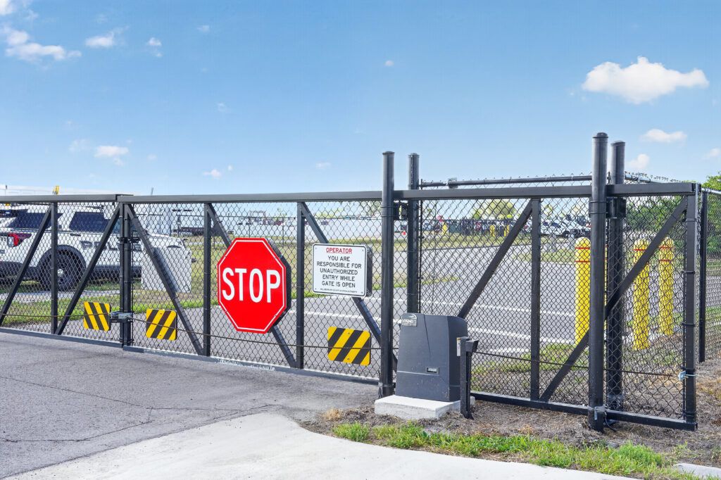 A black metal sliding gate with a red stop sign and a warning sign about unauthorized entry.