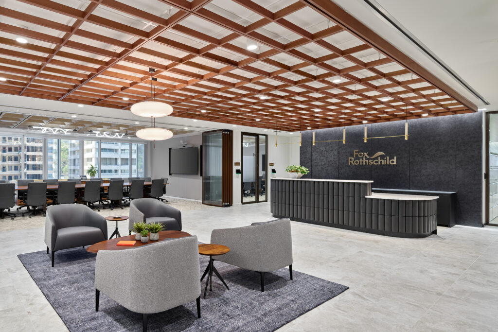 Modern office reception area with a Fox Rothschild branded desk, a lounge seating area with four armchairs, and a conference room in the background.