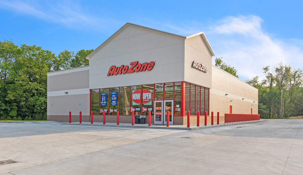 An AutoZone auto parts store with a concrete parking lot and a “Now Open” sign on the front window.