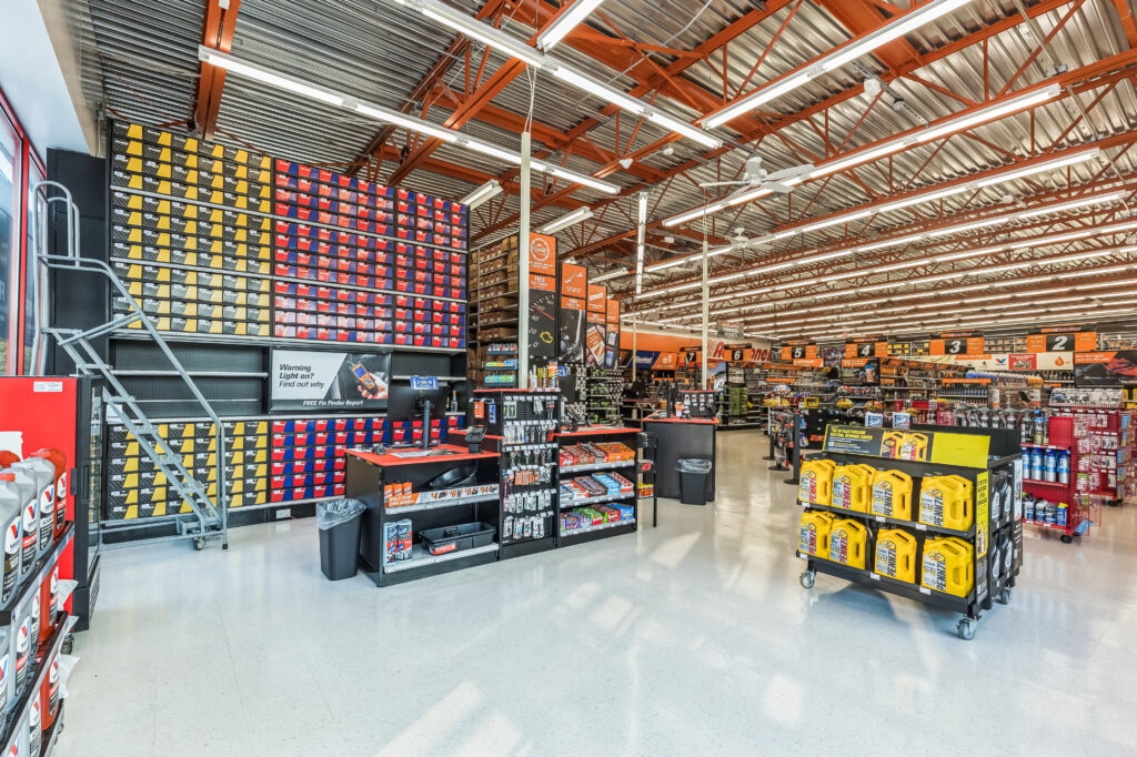 Interior of an automotive supply store featuring shelves of oil bottles, a checkout counter, and a tall display of boxed automotive parts with a rolling ladder.