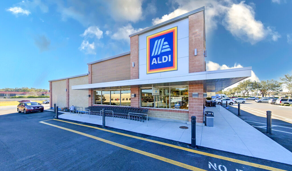 An Aldi grocery store building with a row of shopping carts parked outside under the storefront canopy.