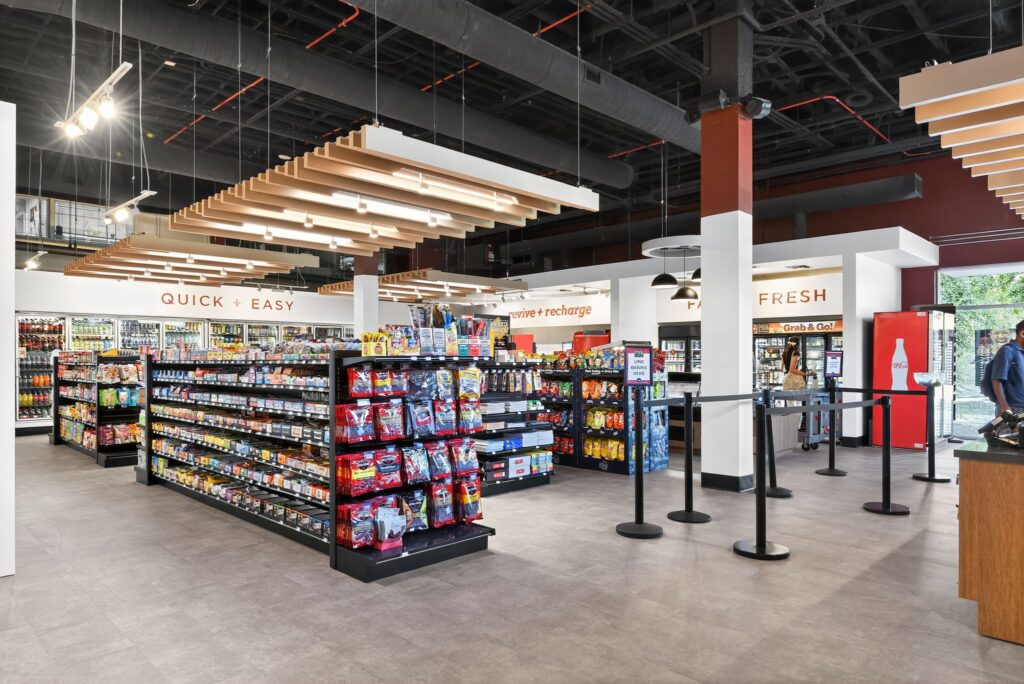 Interior view of a convenience store with aisles of packaged snacks, a “Grab & Go” refrigerated section, and a checkout counter.