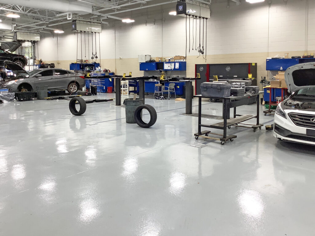 An automotive repair shop with two cars being serviced, a rolling tool cart, and spare tires on the floor.