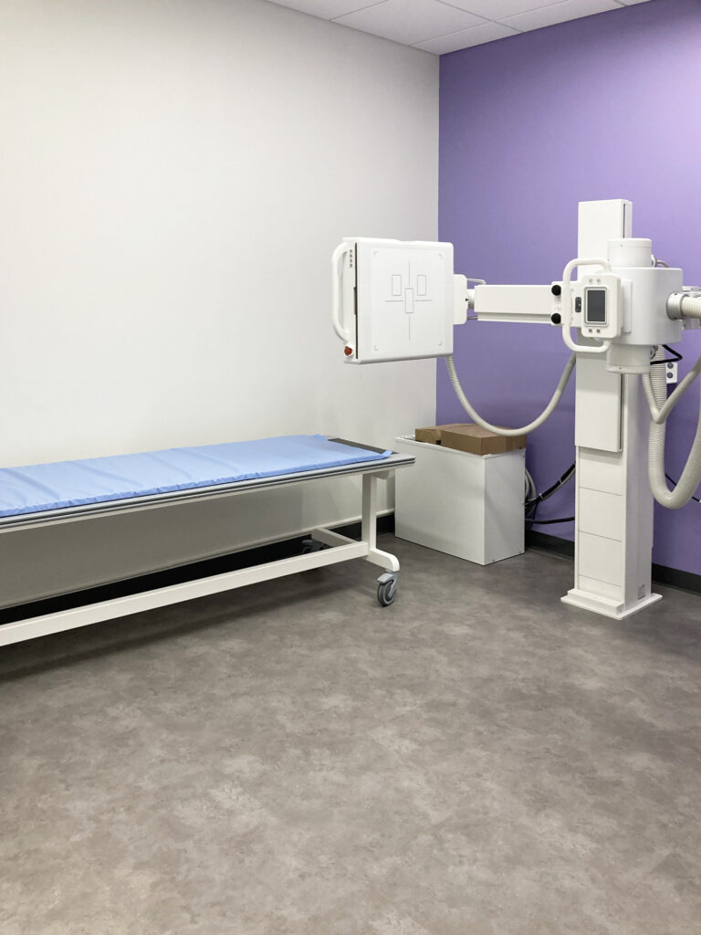 Medical imaging room with an adjustable X-ray machine positioned over a patient exam table.