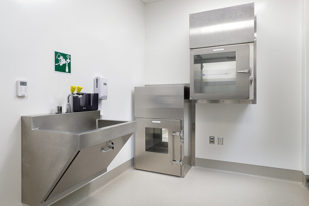 Laboratory room featuring a stainless steel scrub sink, a floor-mounted pass-through chamber, and a wall-mounted BioChemGARD biosafety cabinet.