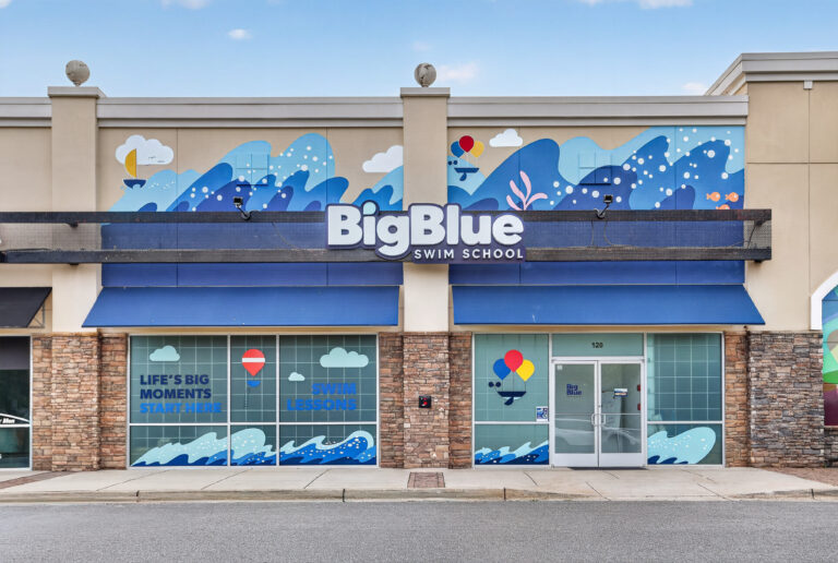 Storefront of a Big Blue Swim School with large blue wave murals and branded window decals.