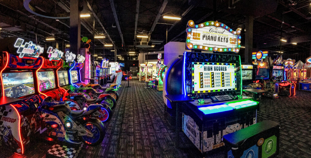 Arcade interior featuring a row of motorcycle racing games on the left and a “Grand Piano Keys” musical arcade game on the right.