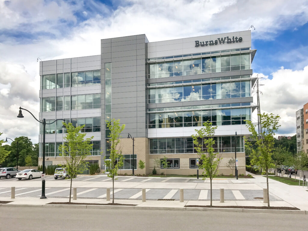 Four-story office building with a glass facade and “BurnsWhite” signage, viewed from a parking lot.