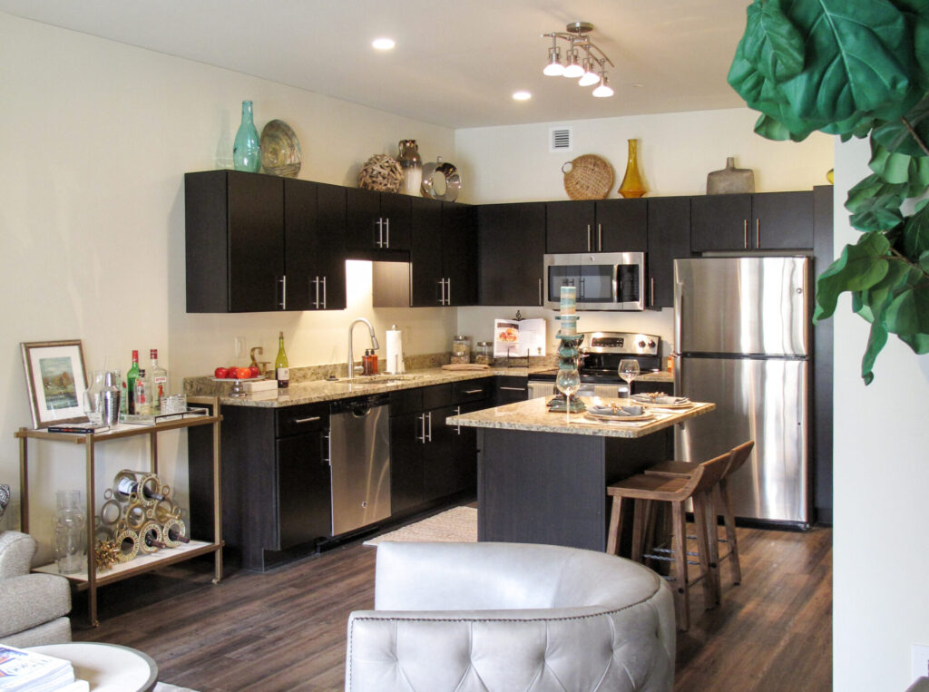 A kitchen with dark cabinets, a granite-topped island, stainless steel appliances, and a bar cart.