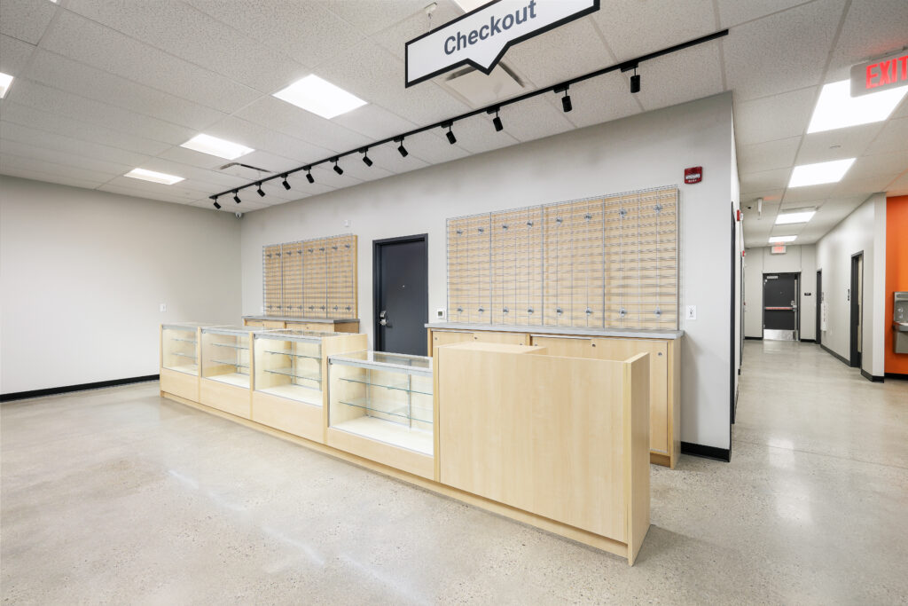 An empty retail checkout area with light wood counters, glass display cases, and grid wall panels.