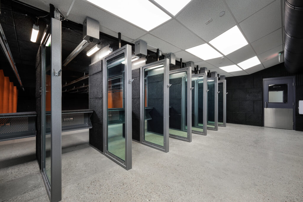 A row of indoor shooting range stalls with glass partitions and acoustic wall panels.