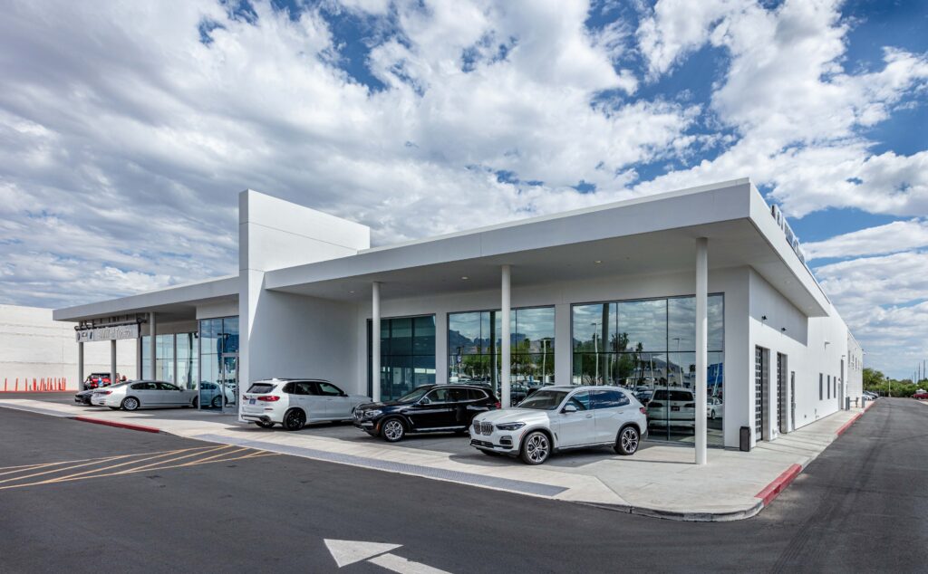 Exterior of a modern BMW car dealership with several luxury SUVs parked in the lot under a cloudy sky.