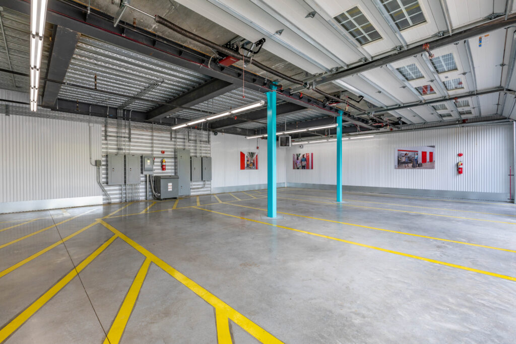 Empty indoor parking area with concrete flooring, yellow painted lines, and two blue support pillars.