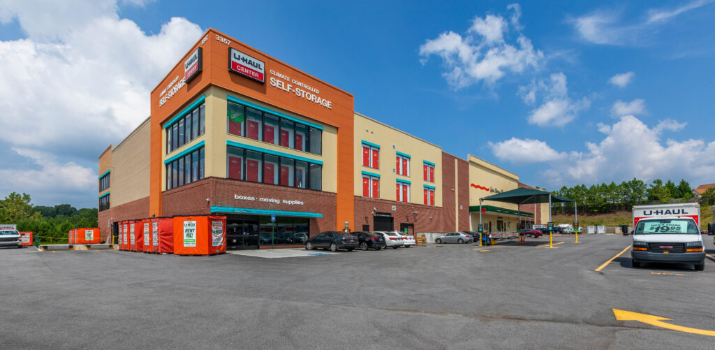 U-Haul self-storage facility with a large parking lot and several parked vehicles under a blue sky.