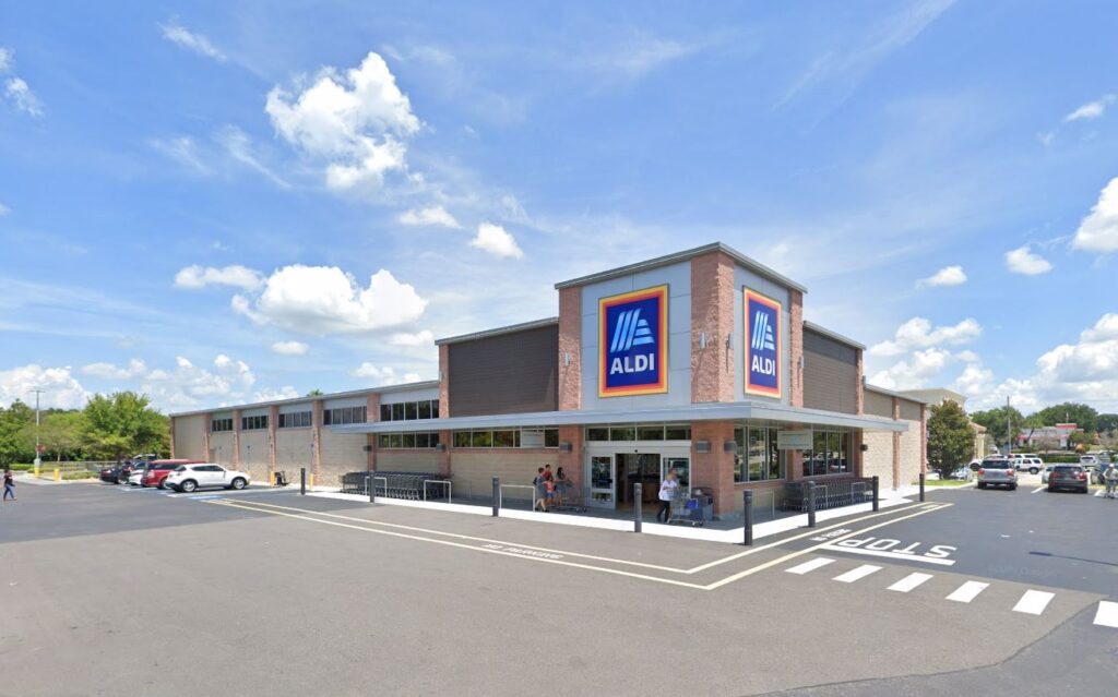 Exterior view of an Aldi grocery store with a parking lot and customers entering the building.