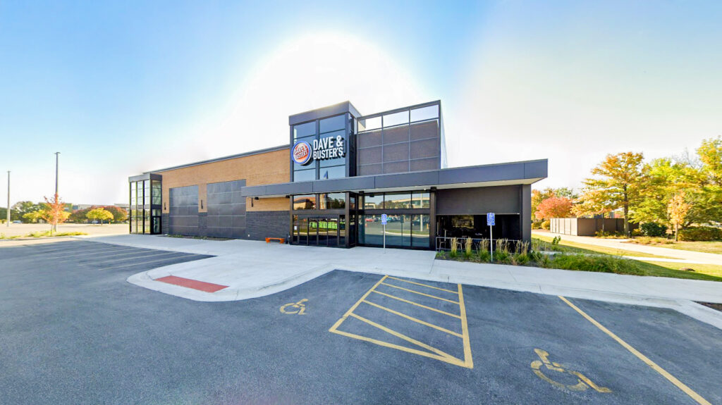 Exterior view of a Dave & Buster’s restaurant building with a large parking lot in the foreground.