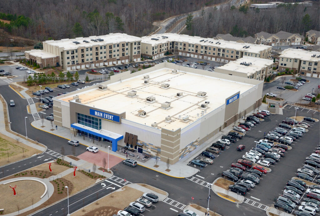 Aerial view of a Main Event entertainment center and surrounding parking lots, situated next to a large residential apartment complex.