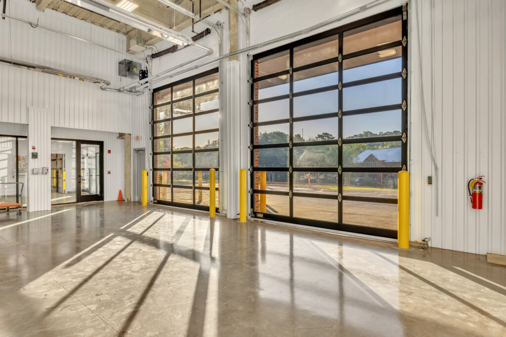 Interior of a commercial garage with two large glass-paneled sectional doors and a fire extinguisher mounted on the wall.