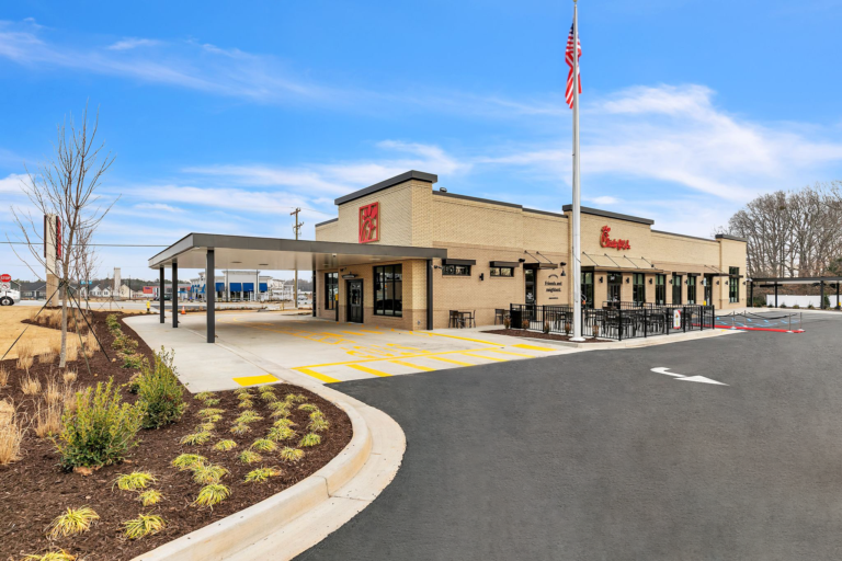Chick-fil-A restaurant with a drive-thru lane, outdoor seating area, and an American flag on a tall pole.