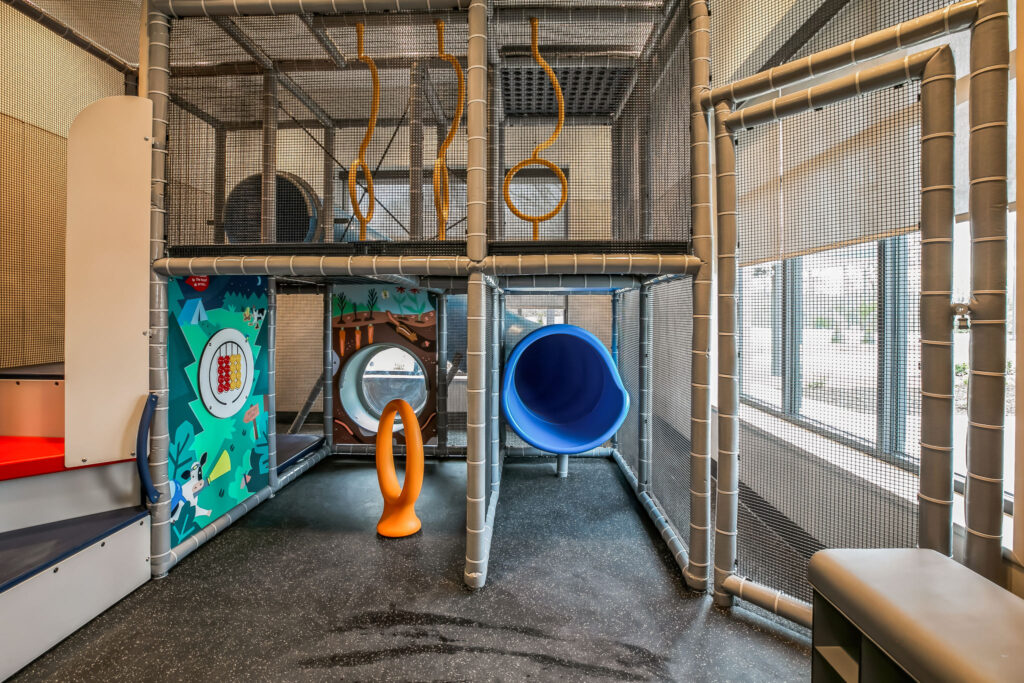 Multi-level indoor playground structure with a blue tunnel slide, climbing obstacles, and activity panels.