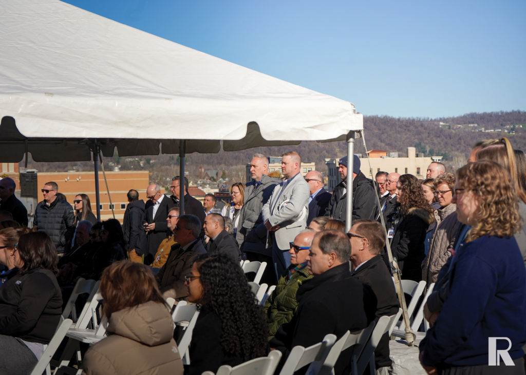 A crowd of people sitting and standing under a white canopy at an outdoor event.