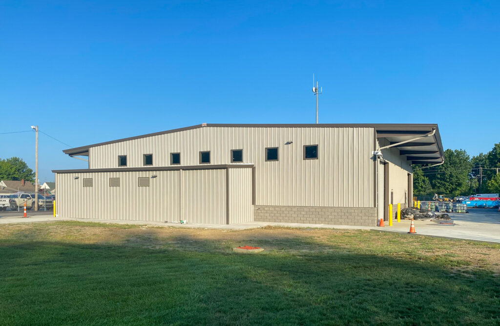A beige metal industrial building with a single-slope roof, small square windows, and a loading bay.