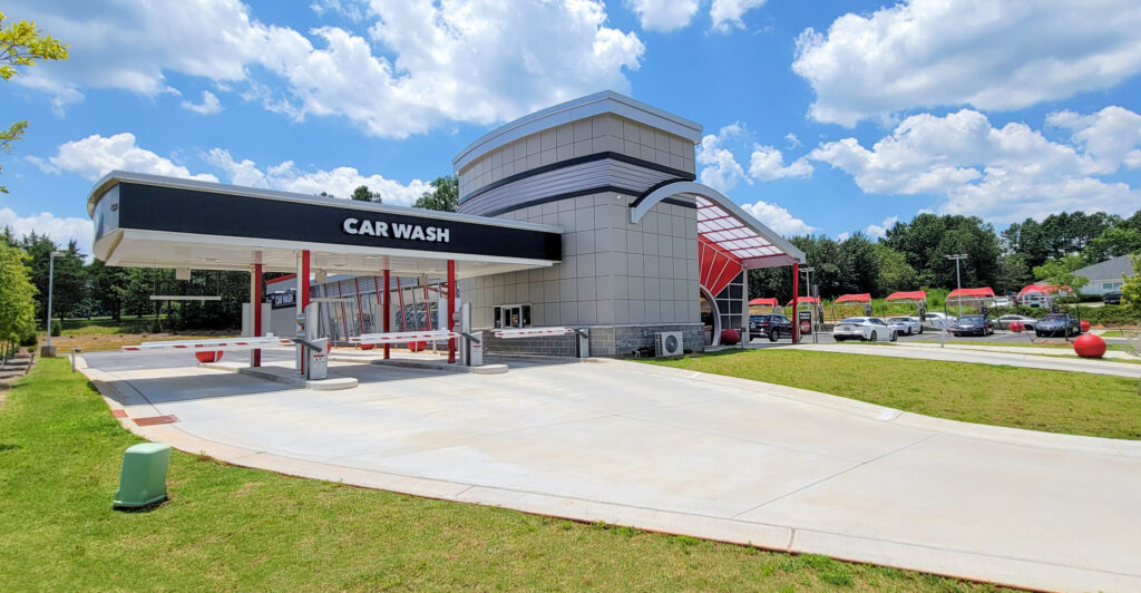 A modern drive-through car wash facility under a blue, cloudy sky.