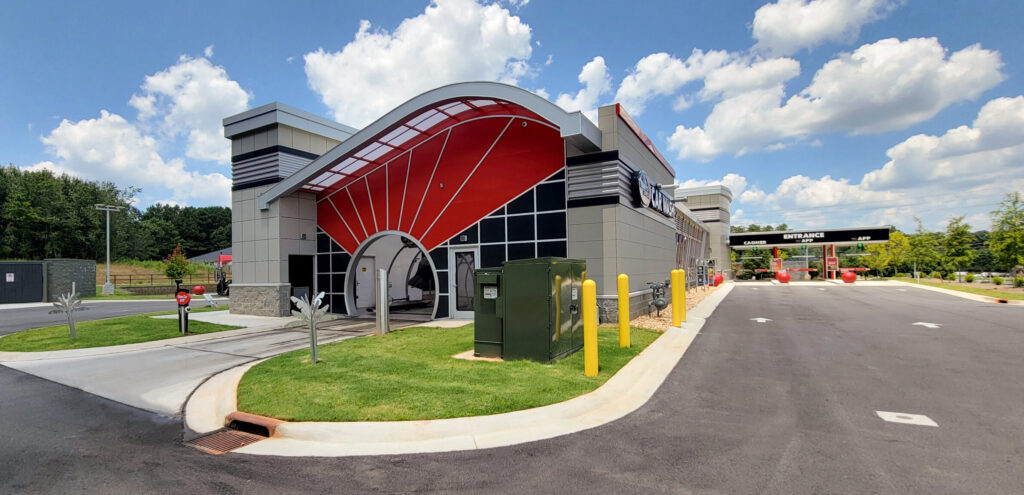 Modern car wash facility with a red-accented entrance arch and a separate drive-through entrance lane.