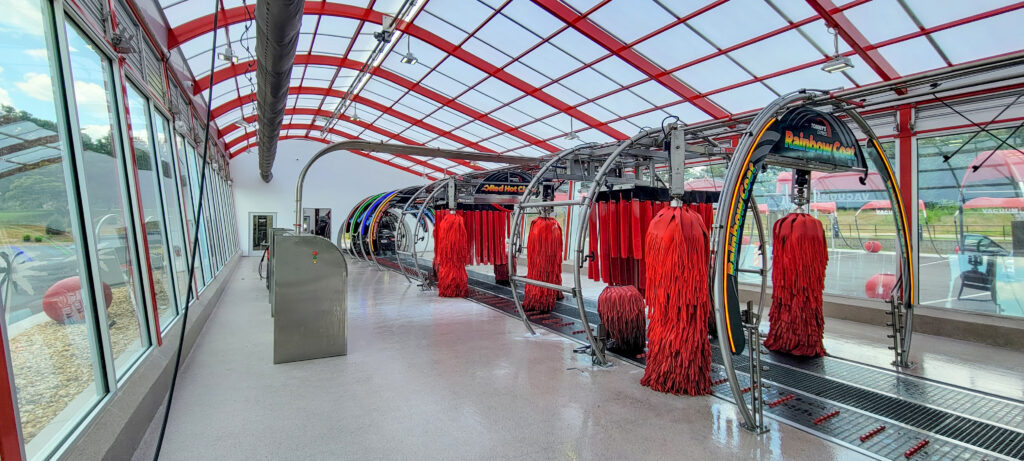 Interior of a car wash tunnel with red rotating cleaning brushes and a glass ceiling.