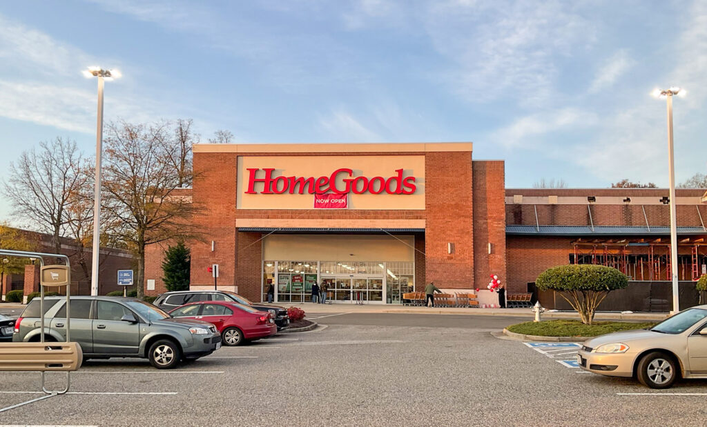 Exterior view of a brick HomeGoods store with a “Now Open” sign above the entrance and a parking lot in the foreground.