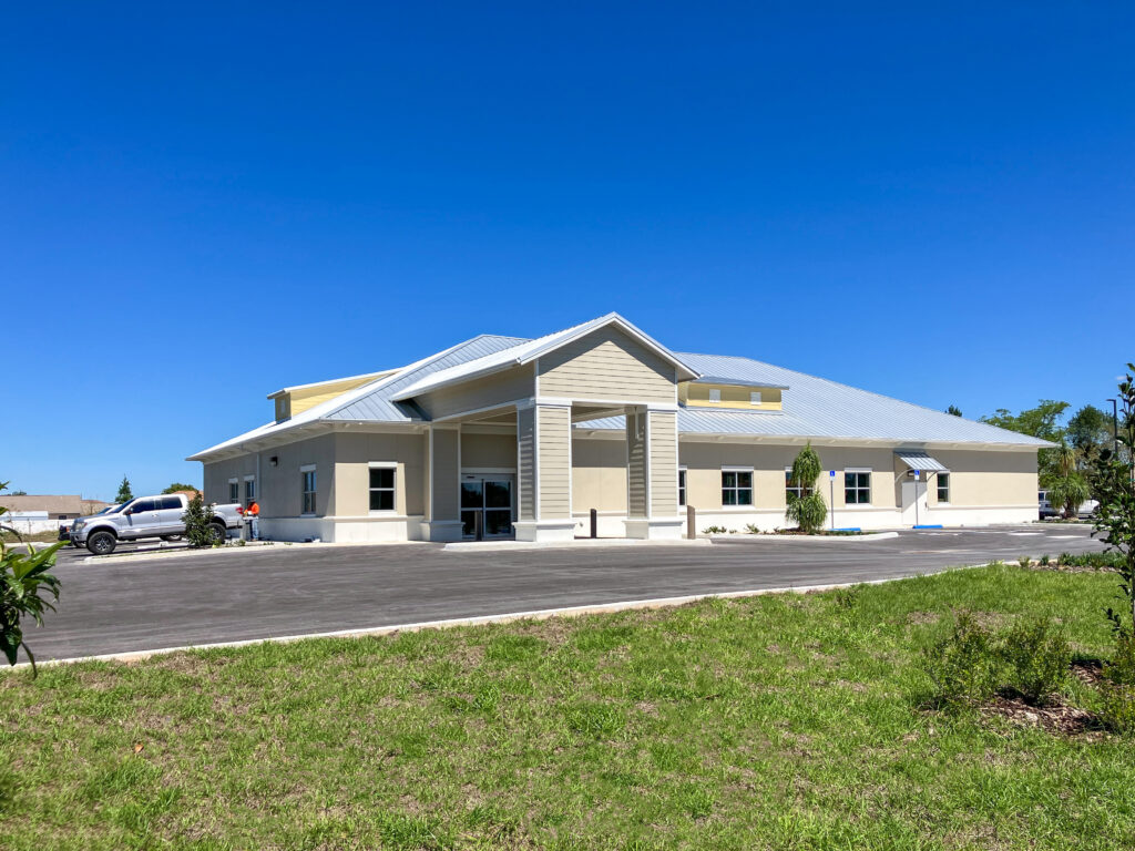 A single-story commercial building with a beige facade, a metal roof, and a covered entryway, set against a clear blue sky.