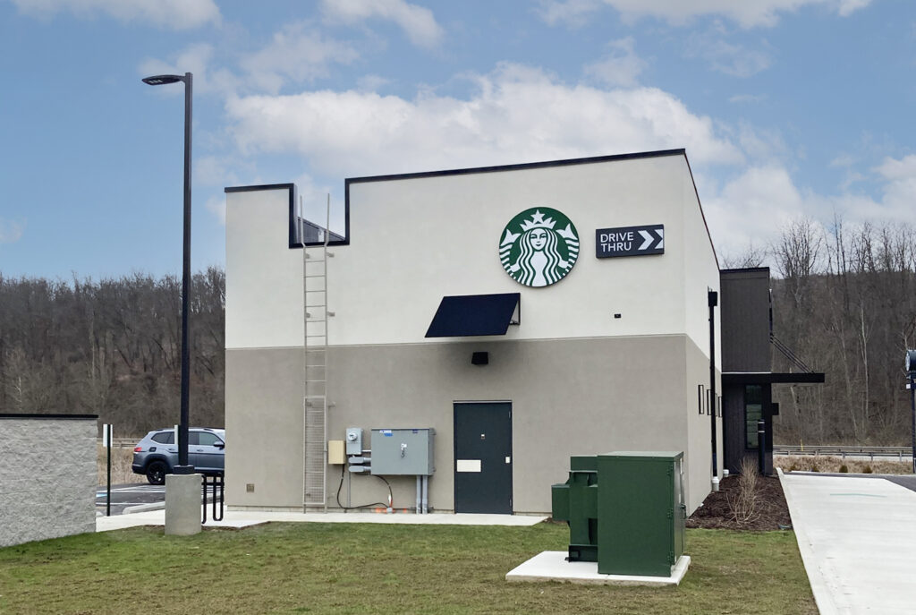 Side view of a Starbucks building with a circular company logo and a drive-thru directional sign on the wall.