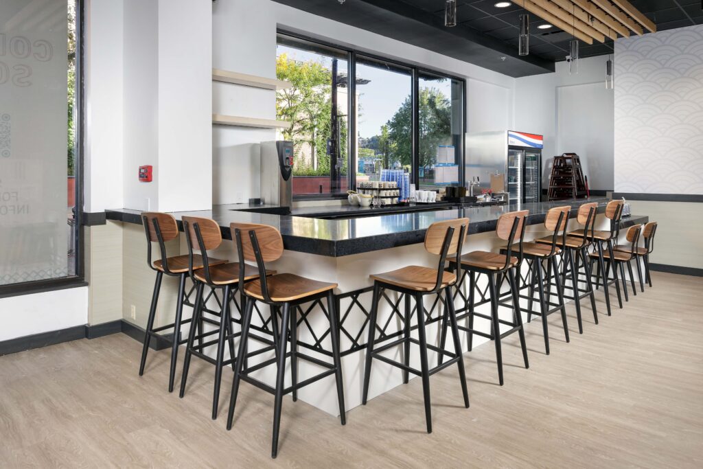 A row of wooden bar stools lined up along a black countertop in a modern restaurant.