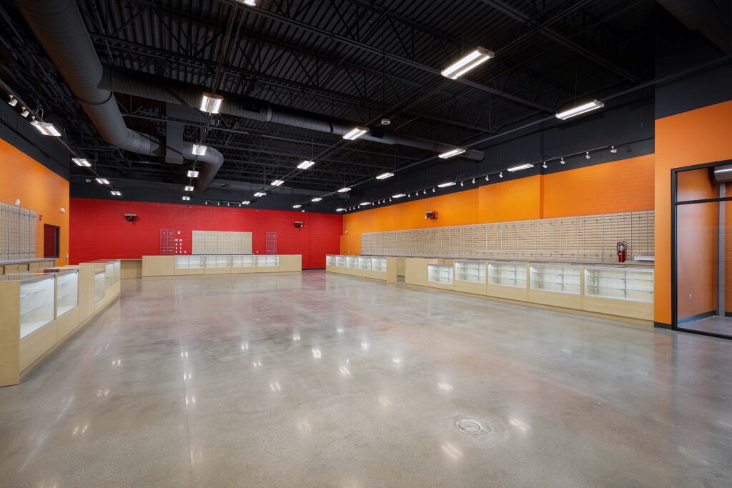Empty retail space with glass display cases lining red and orange walls under an exposed black ceiling.